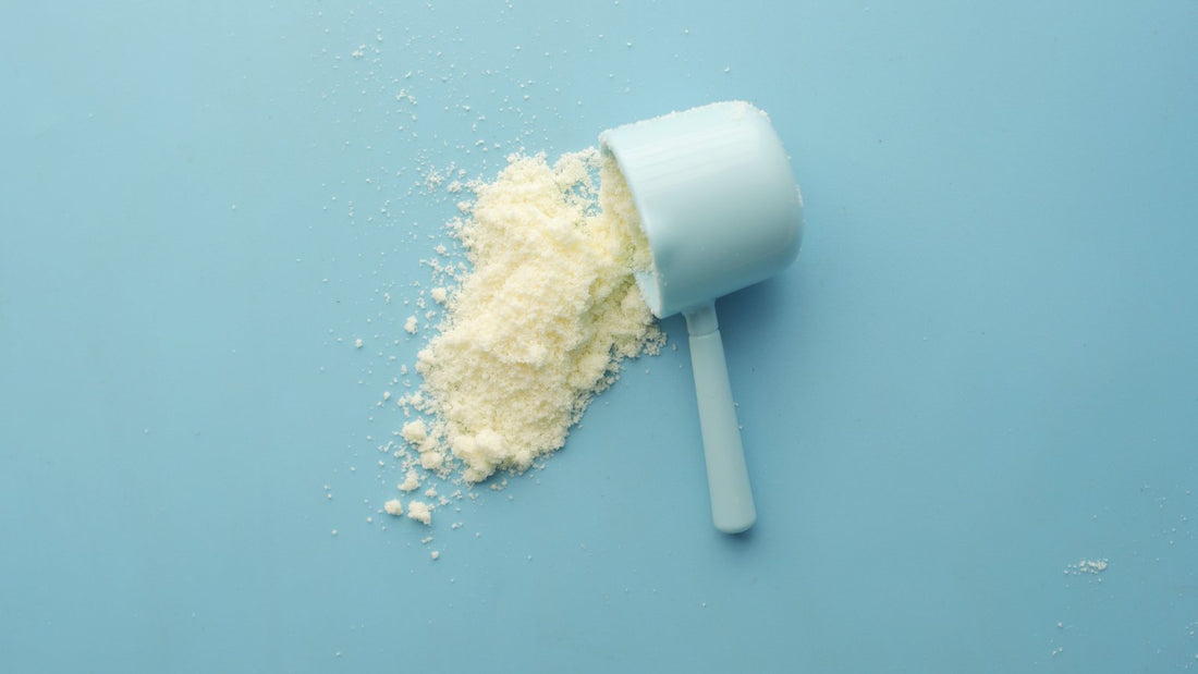 Un scoop de plástico volcado sobre una superficie azul claro, con el polvo blanco derramado a un lado